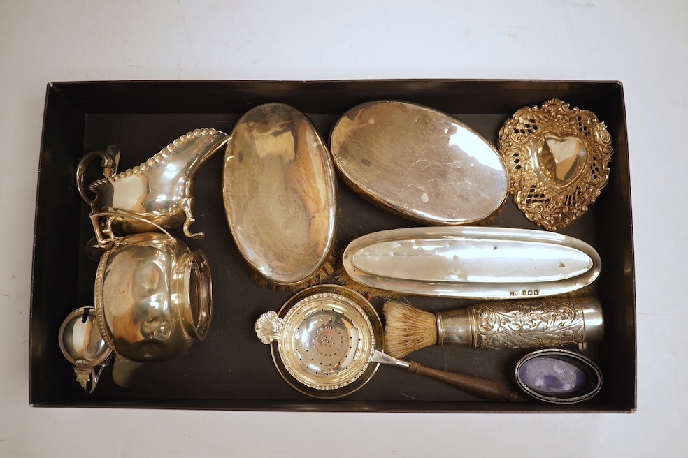 A small quantity of assorted silver including a Victorian sauceboat, London, 1851, length 12.6cm, a sugar bowl, a tea strainer on stand, mustard pot and ladle, three mounted brushes, a salt, pieced bonbon dish and a case